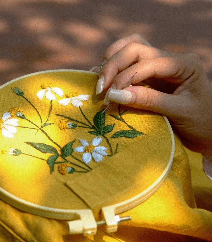 Hands threading an embroidery needle with floss and a long thread tail
